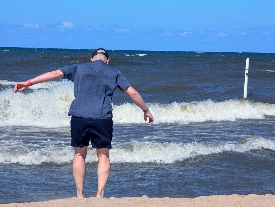 Kevin facing the blue waters of Lake Michigan, with the white waves crashing and wind blowing.